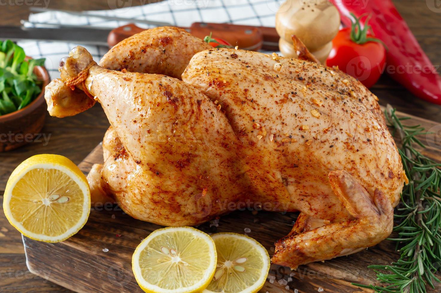 pollo asado entero con limón y verduras en tabla de cortar. fondo rústico de madera foto