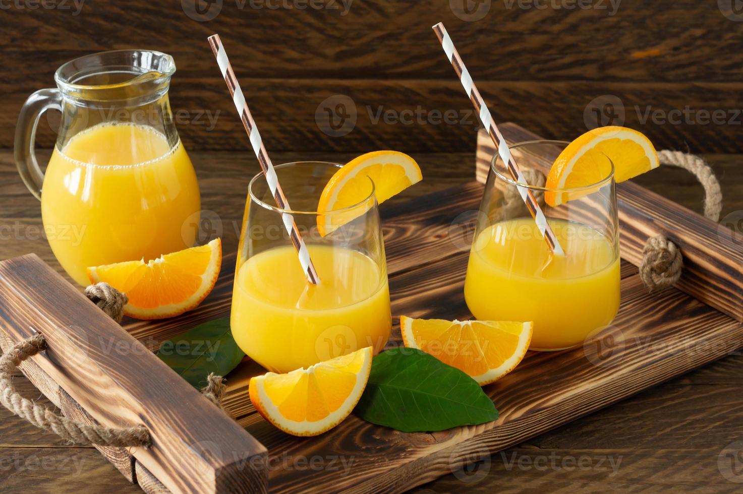 jugo de naranja fresco en vasos con naranjas cortadas en bandeja de madera. bodegón rústico con cítricos foto