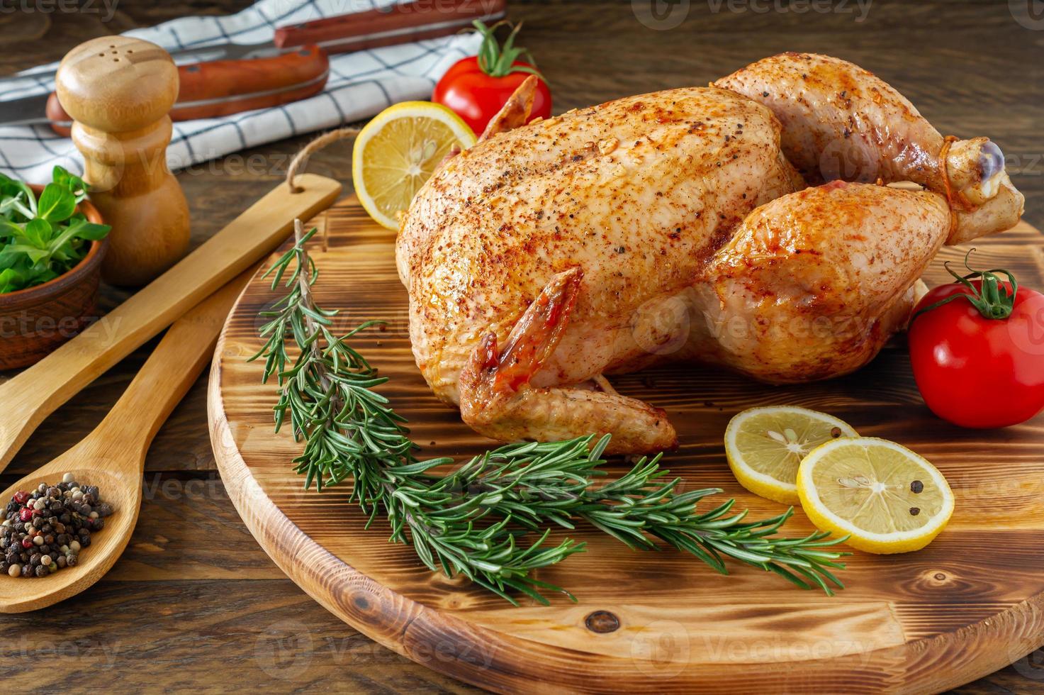 Whole grilled chicken with caramelized skin and fresh rosemary on a wooden dinner table. photo