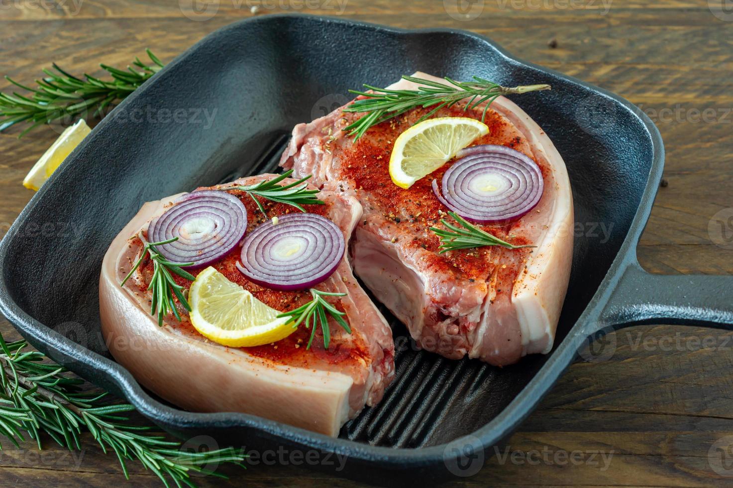 Pieces of raw pork steak with spices and herbs rosemary, salt and pepper in grill pen on wooden background in rustic style photo