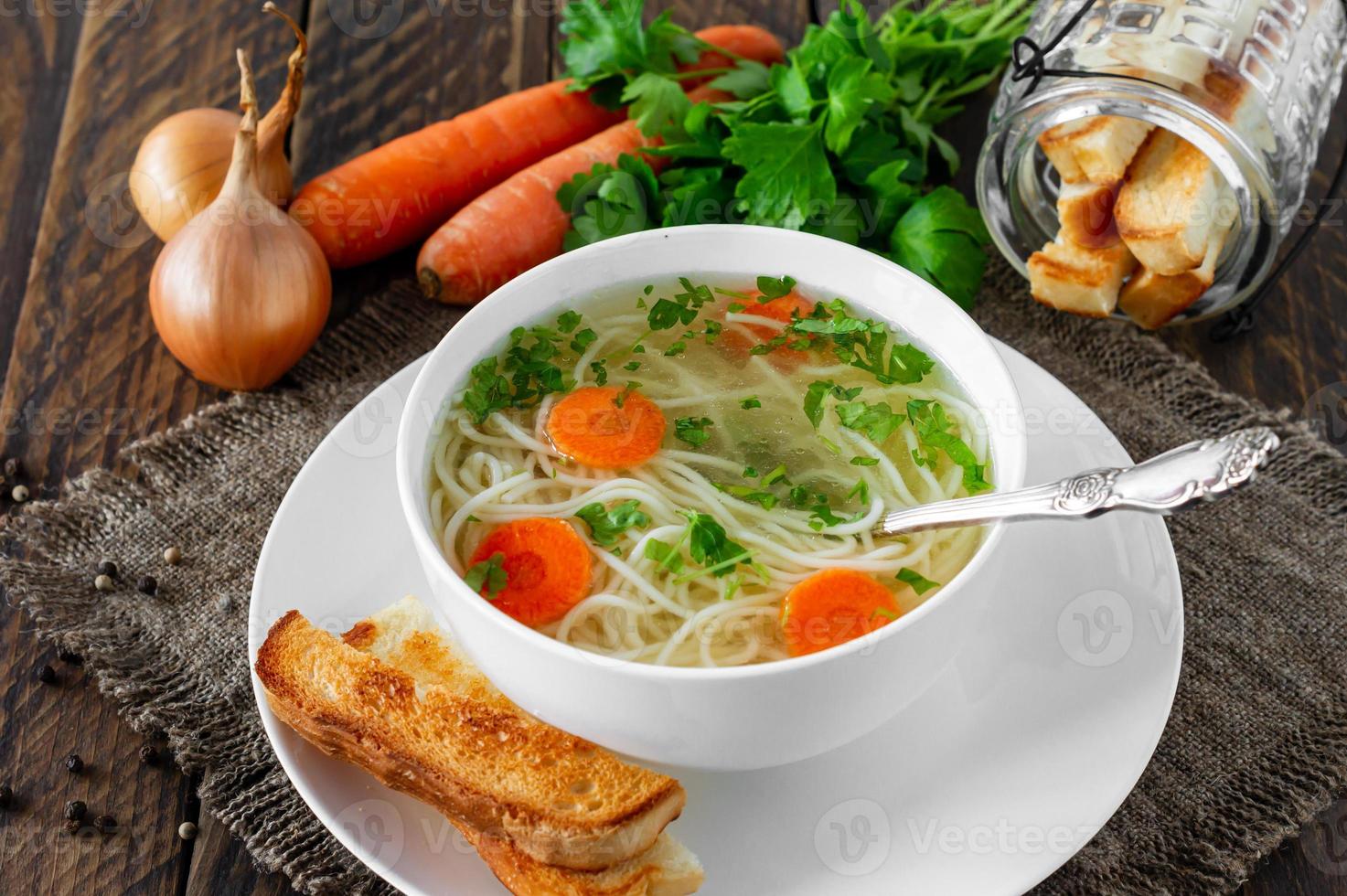 Chicken broth with parsley in a white bowl and croutons on a rustic wooden background. photo