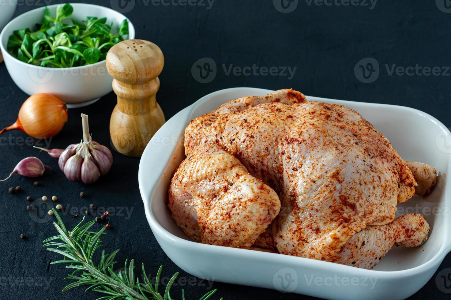 Whole raw chicken with herbs and spices ingredients on dark background ready to cook photo