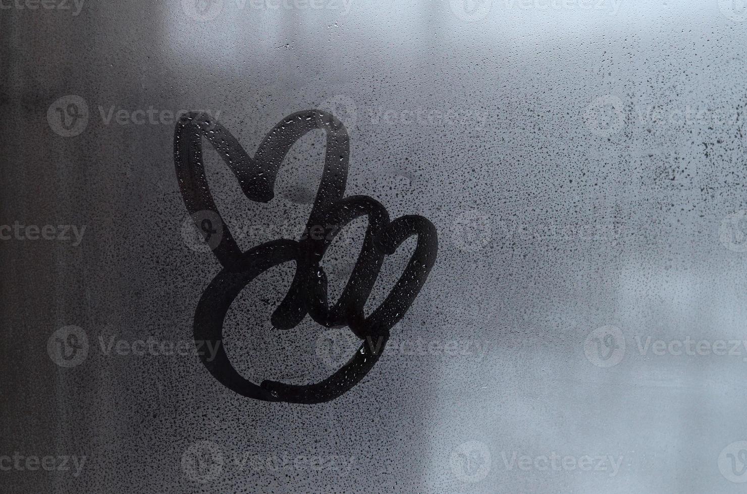 The image of the peace symbol is drawn with a finger on the surface of a misted glass window. Combination of two fingers photo