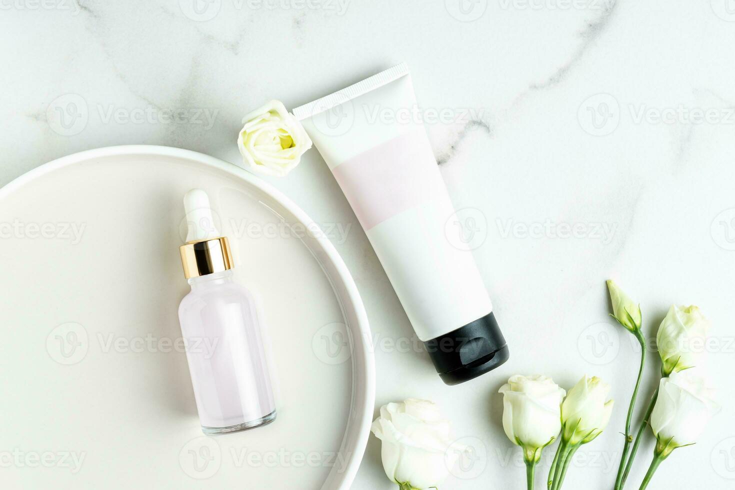 top view of cosmetics set - beauty face oil in dropper bottle and unbranded tube with cream or mask on marbal table with eustoma flowers. Trendy flat lay stillife photo