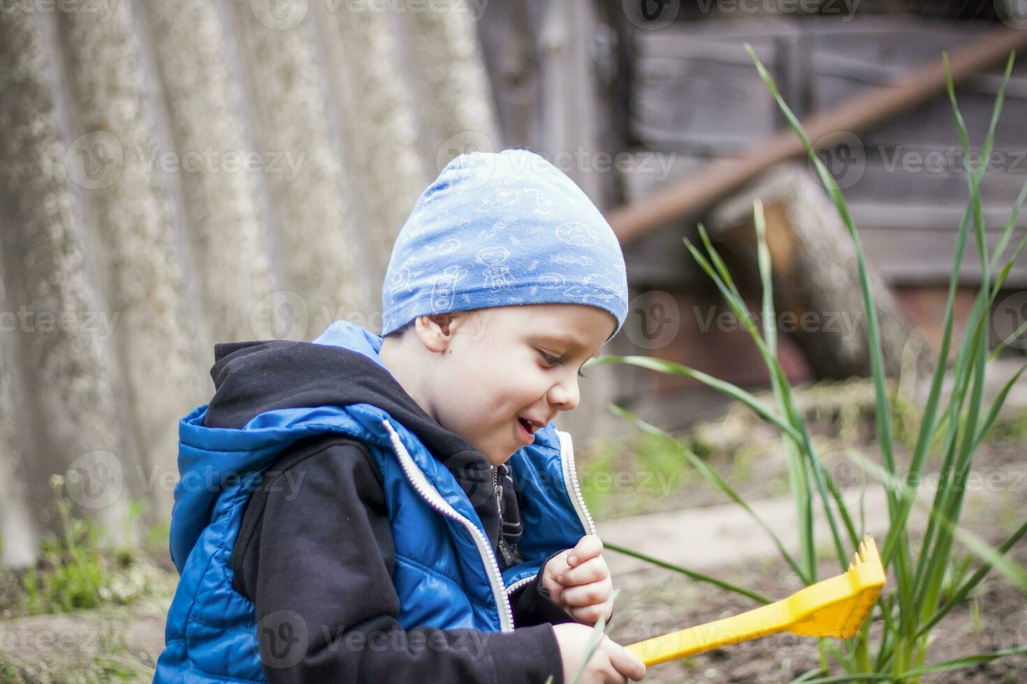 A child is planting a garden. A child's rake in his hands. A little gardener boy is planting plants in a flower bed. Gardening tools in the hands of a child. photo