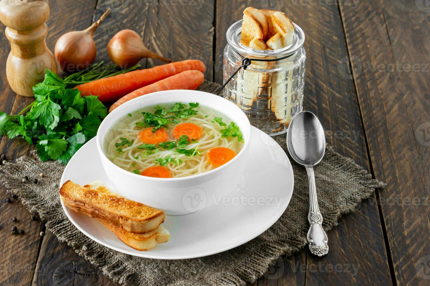 Chicken bouillon in the white bowl on the rustic wooden background served with croutons. photo