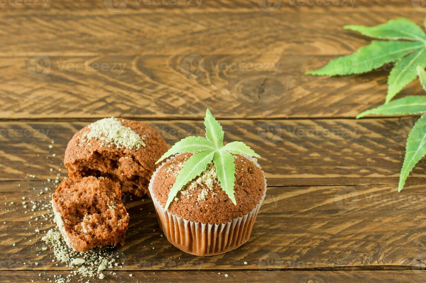 Healthy and tasty vegan and gluten free muffins topped with hemp seeds on a white plate on wooden table. Marijuana cupcake muffins with cannabis leaves photo