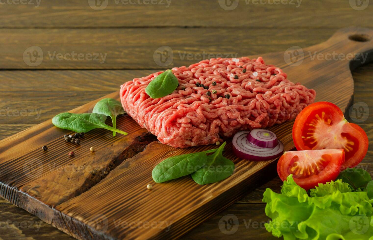 Raw minced beef meat on a wooden cutting board with vegetables and spices. Cooking and healthy eating concept. photo