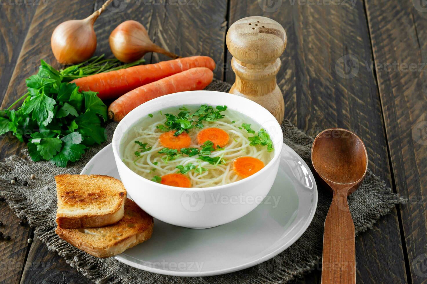 Fresh bouillon in a white bowl with finely chopped herbs with parsley and garlic on a wooden table. Hot soup made from chicken meat, carrots, onions, garlic, parsley and pepper. photo