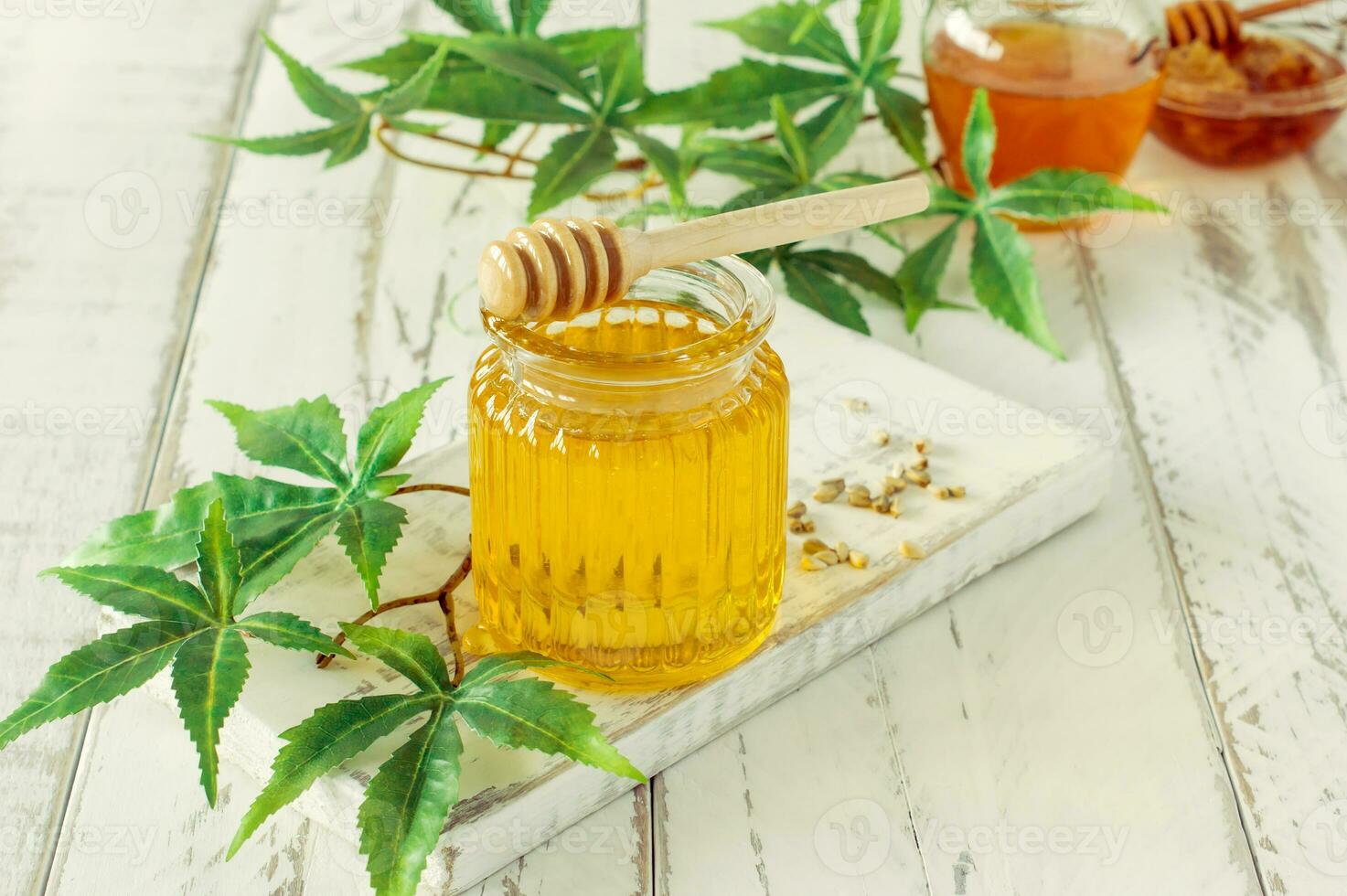 glass jar of honey, wooden dipper and hemp leaves close-up on wooden background. CBD healthy products. Sweet dessert. Alternative medicine photo