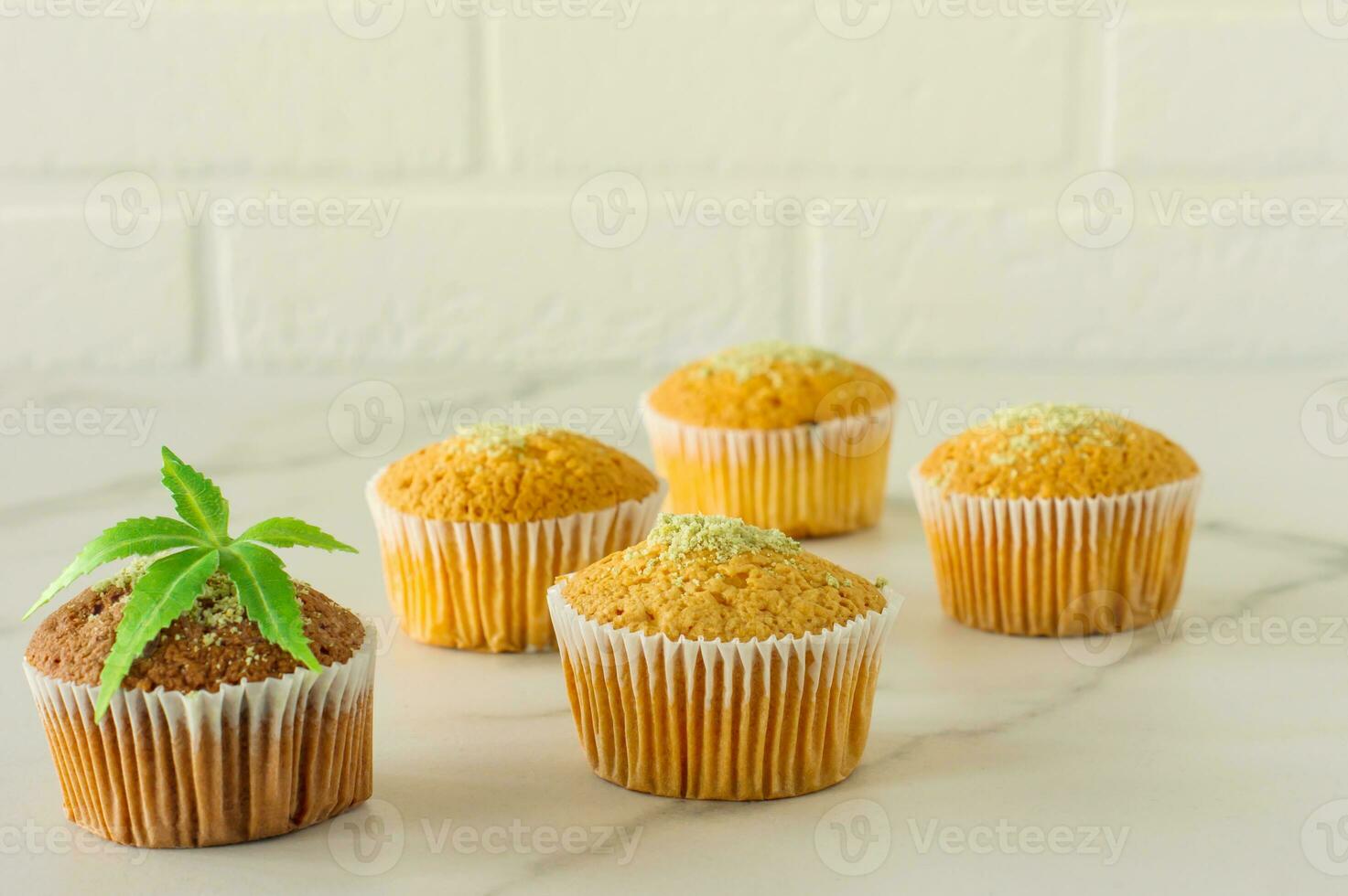 Healthy and tasty vegan and gluten free muffins topped with hemp seeds on a marble table. Marijuana cupcake muffins with cannabis leaves photo