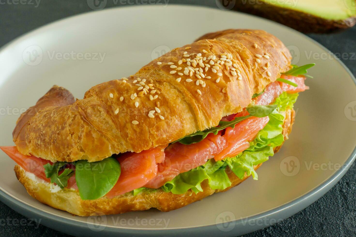 croissant sandwich with salmon, ricotta cheese and arugula on a plate on a dark background. Side view close up photo