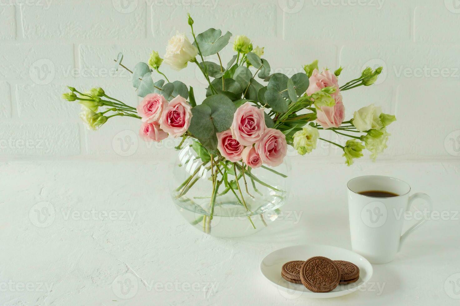 bouquet of Roses, eustoma and eucalyptus in a glass stylish vase on a table. Flowers composition for interior decoration. photo