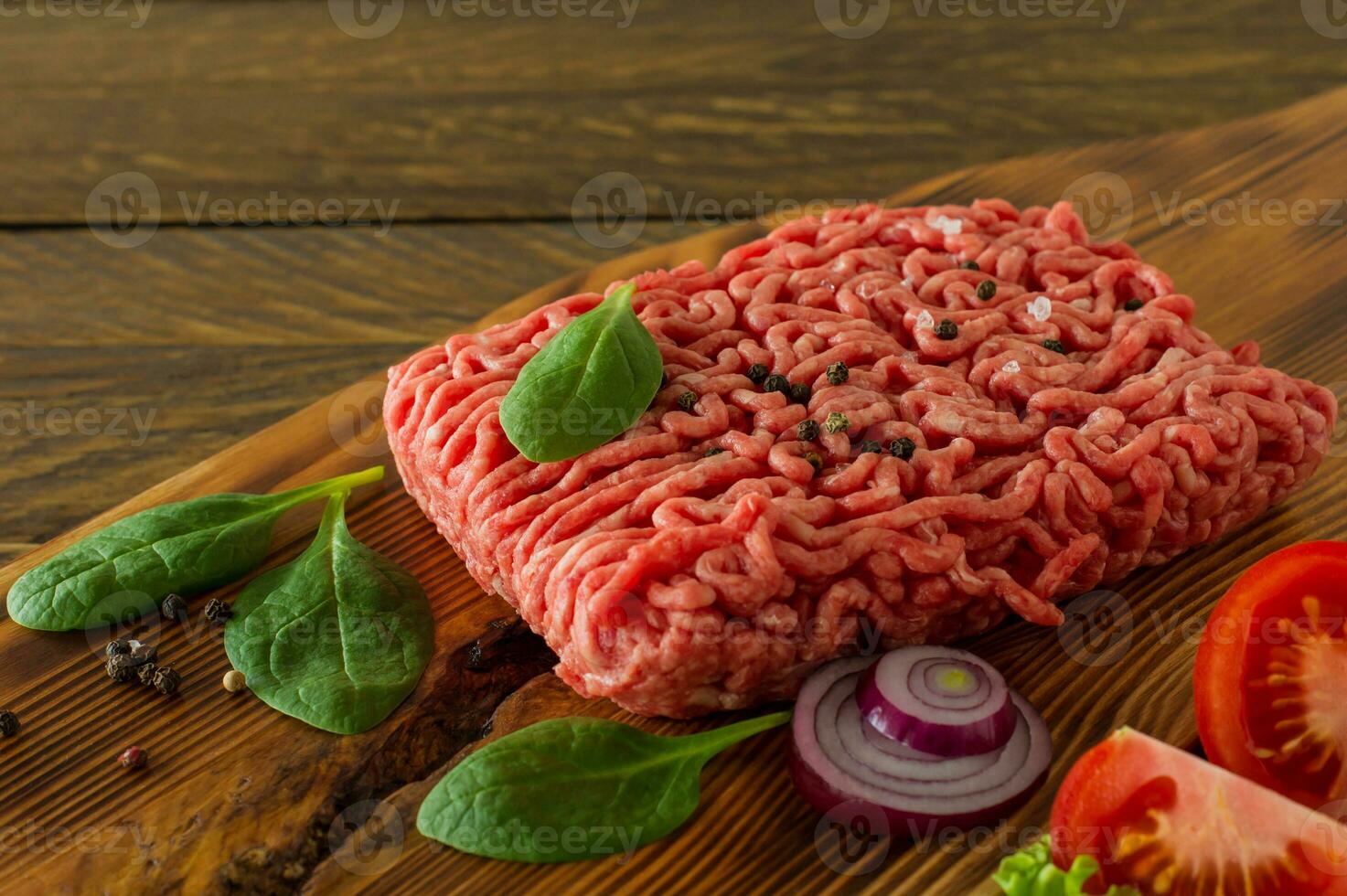 Raw minced beef meat on a wooden cutting board with vegetables and spices. Cooking and healthy eating concept. photo