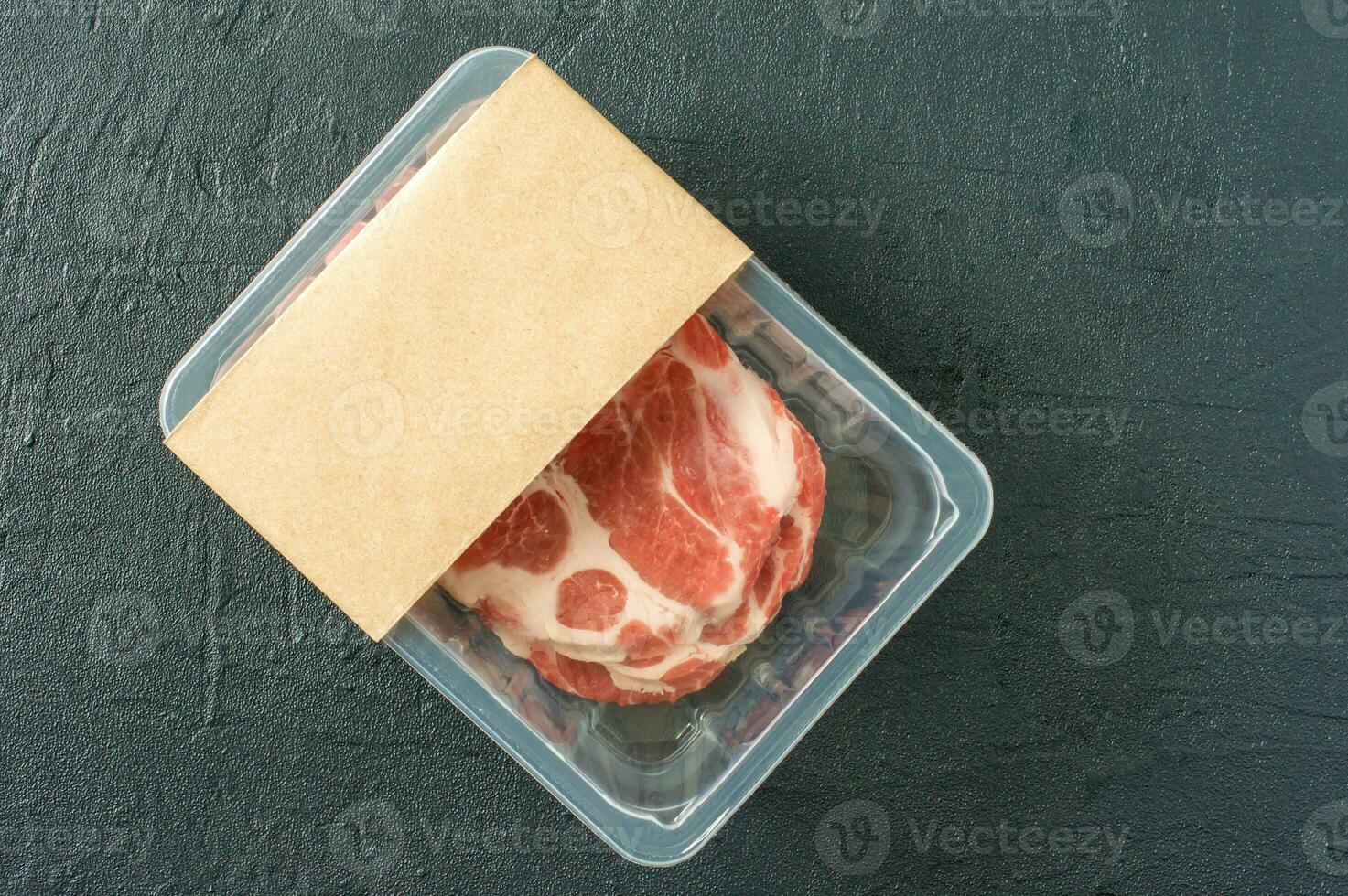 Raw marbled pork steak in vacuum packaging on black background, top view, logo mockup for design photo