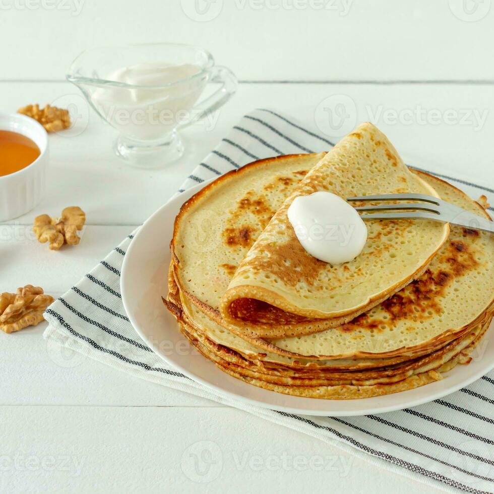 Pancakes served with honey syrup and sour cream on a white plate. Traditional crepes for pancake week or Shrovetide. photo