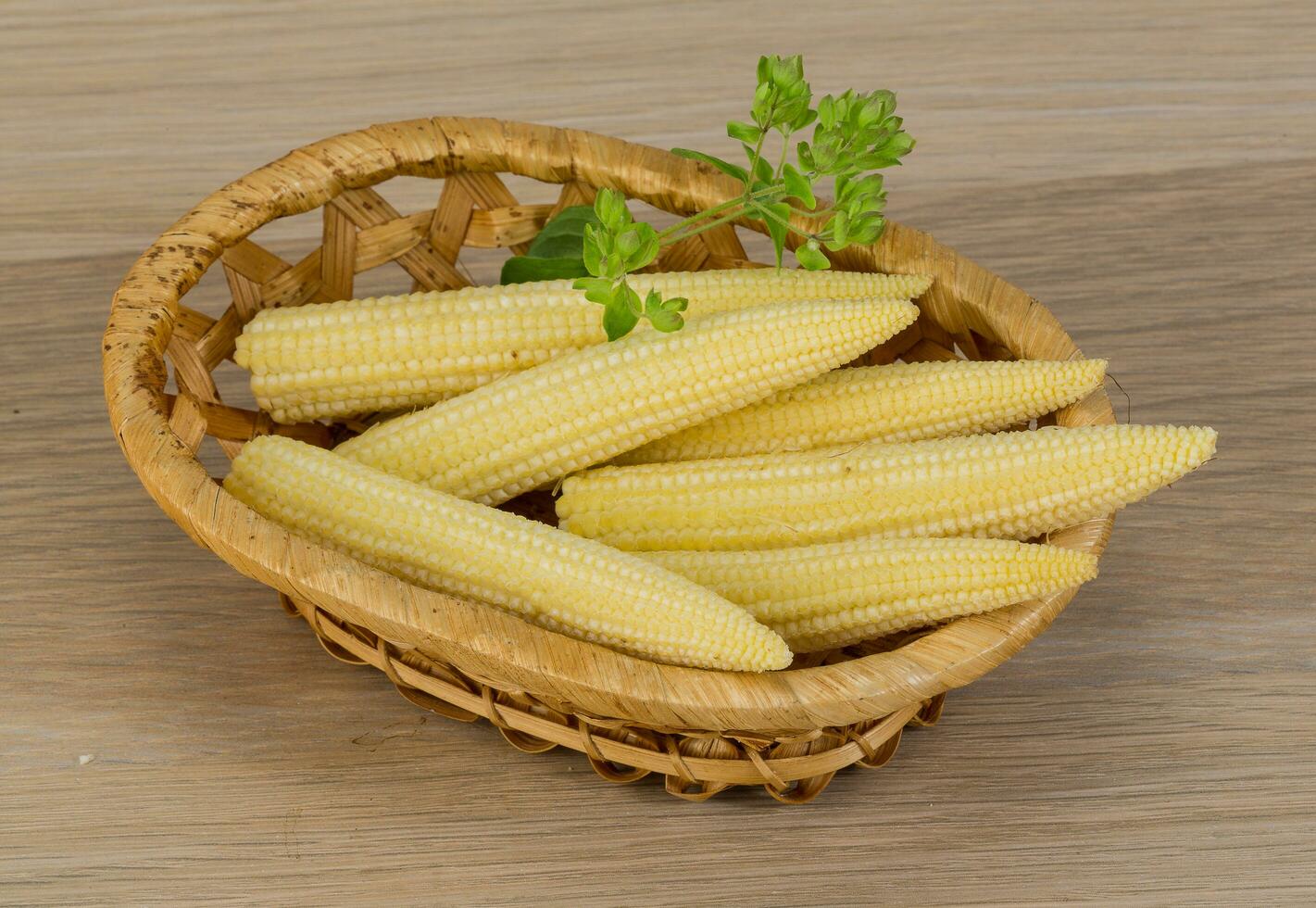 maíz tierno en una canasta sobre fondo de madera foto