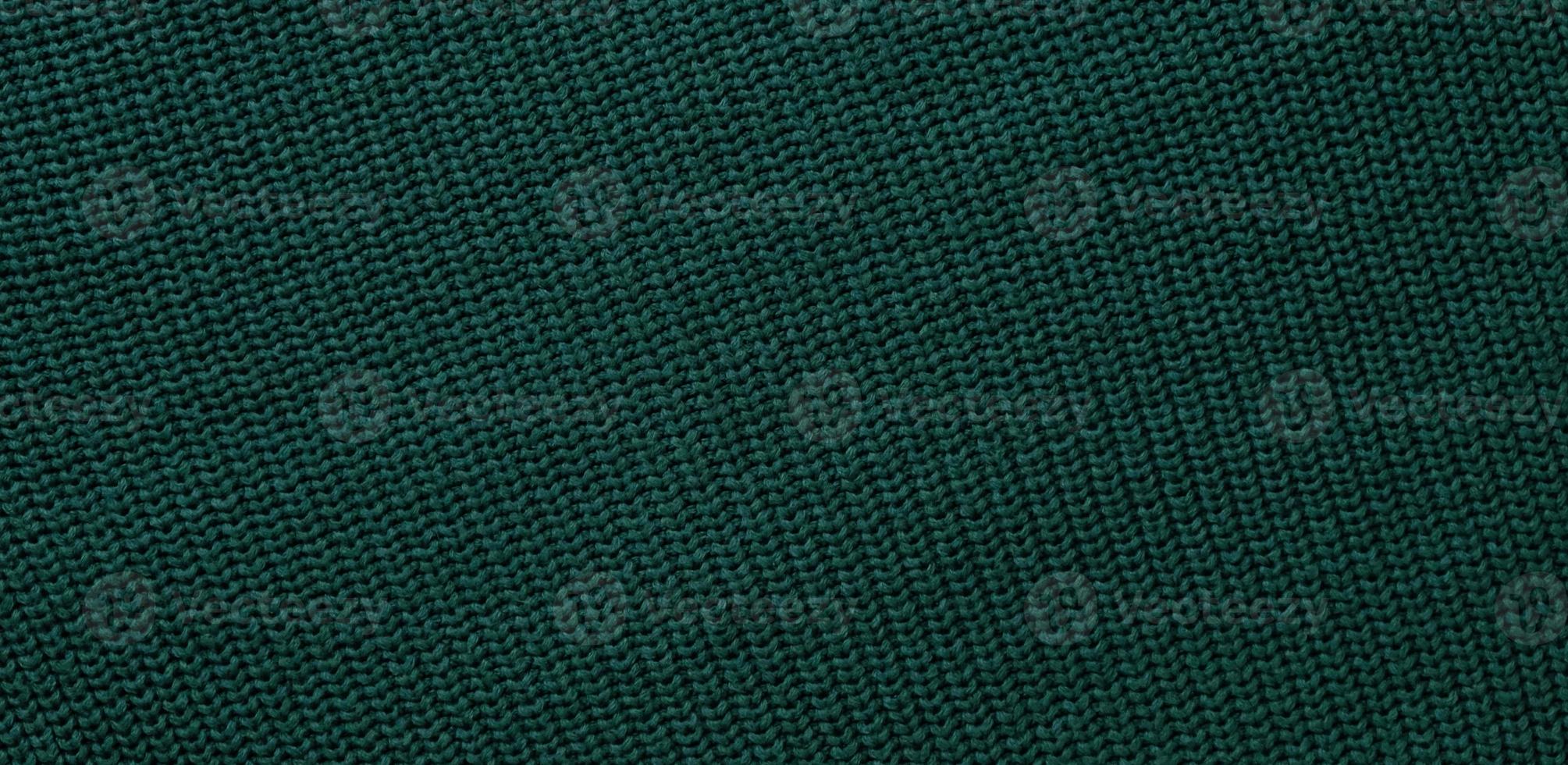 Texture of smooth knitted dark green sweater with pattern. Top view, close-up. Handmade knitting wool or cotton fabric texture. Background of Large Ribs knit pattern with knitting needles or crochet. photo