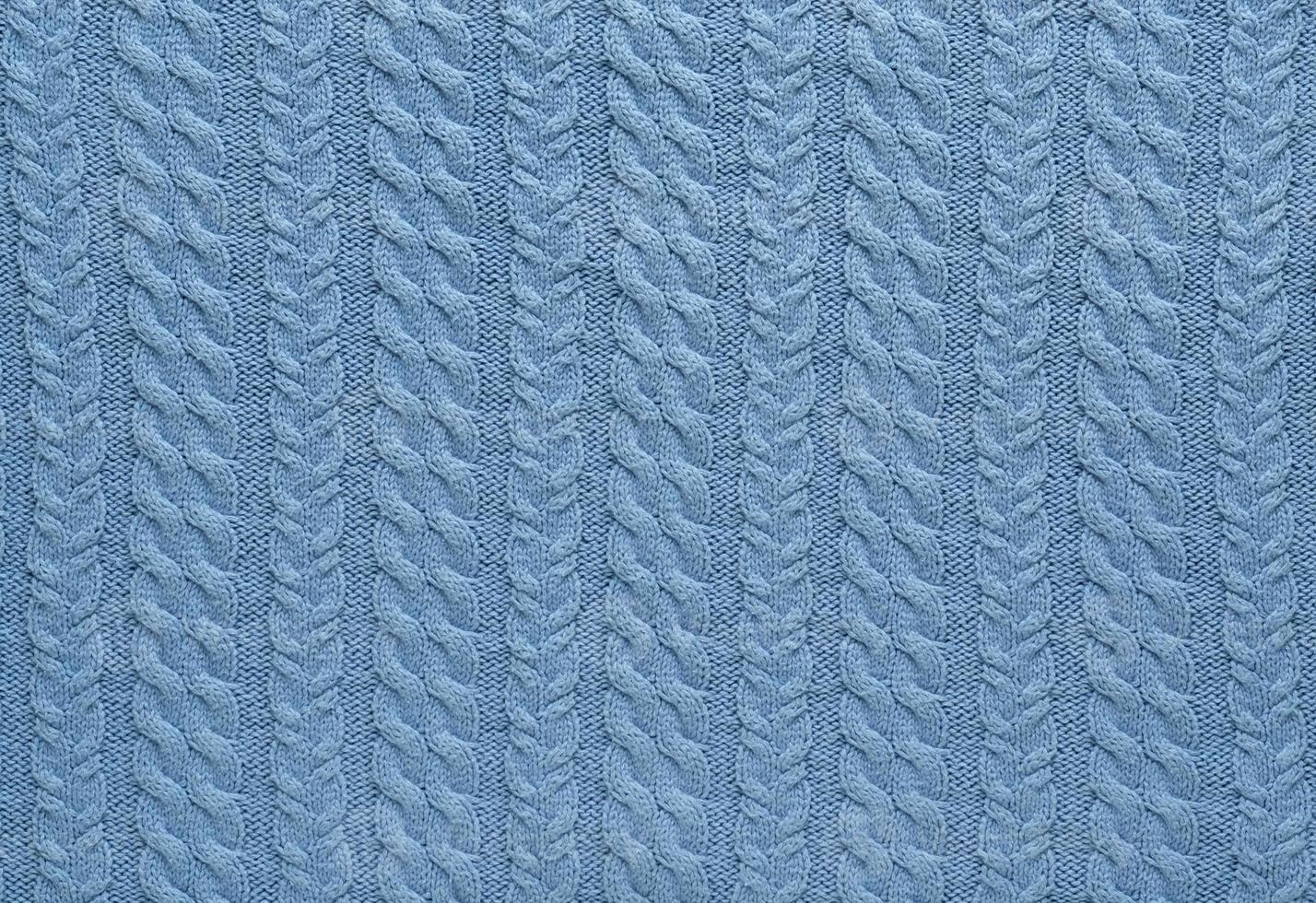 Texture of smooth knitted blue sweater with pattern. Top view, close-up. Handmade knitting wool or cotton fabric texture. Background of knitting patterns with a vertical Braid Cable. photo