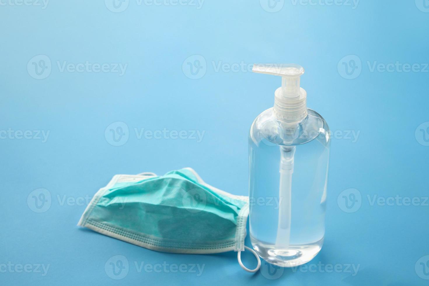 Alcohol hand sanitizer gel bottle with surgical face mask on blue background protection against COVID-19 coronavirus. Healthcare and medical concept photo