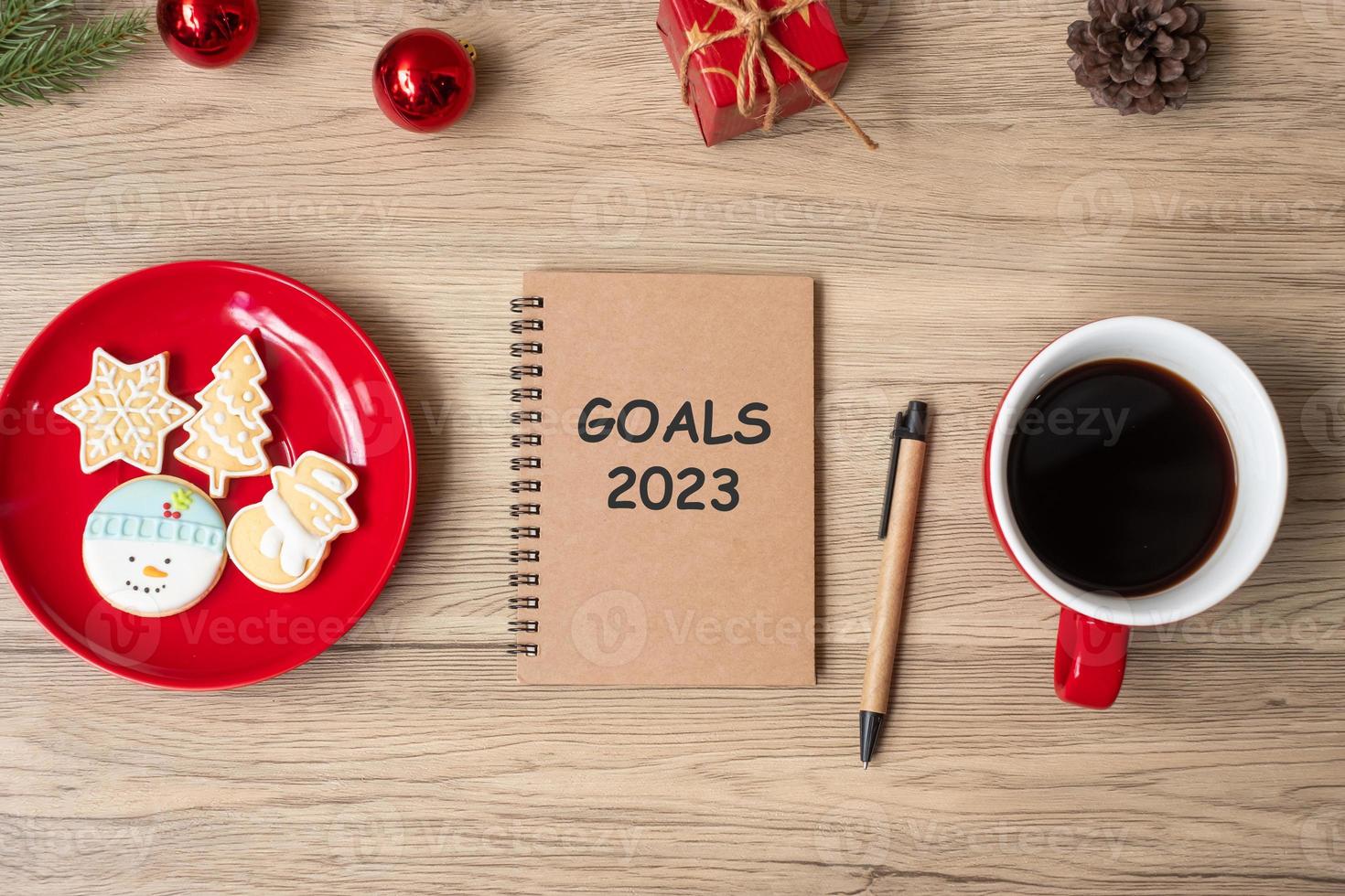 Meta 2023 con cuaderno, taza de café negro, galletas navideñas y bolígrafo sobre mesa de madera. navidad, feliz año nuevo, resolución, lista de tareas, estrategia y concepto de plan foto