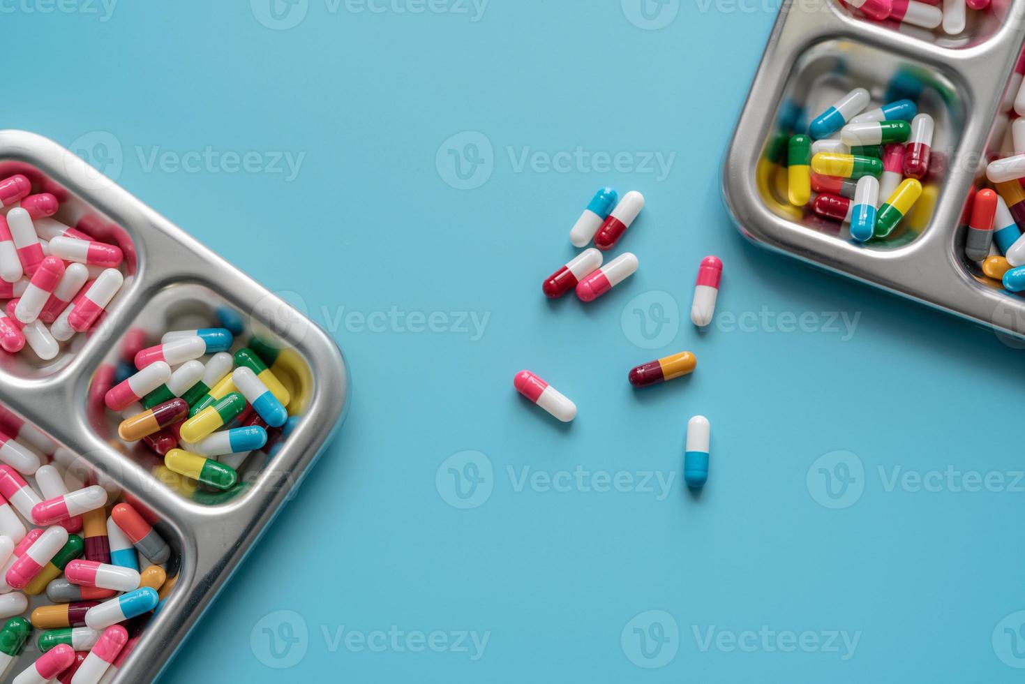 Multi-colored capsule pills in stainless steel tray and on blue background. Pharmacy banner. Pharmaceutical industry. Pharmaceutics. Prescription drugs. Medical and healthcare. Drug related problems. photo