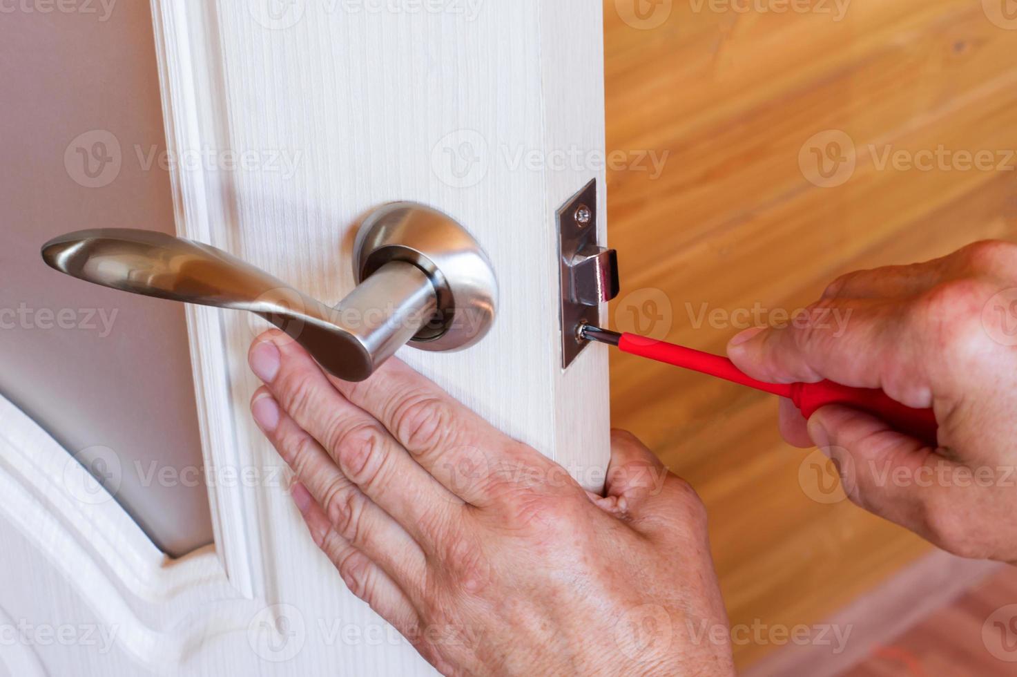 carpenter repairs the front door lock. fastens the handle with a screwdriver. photo