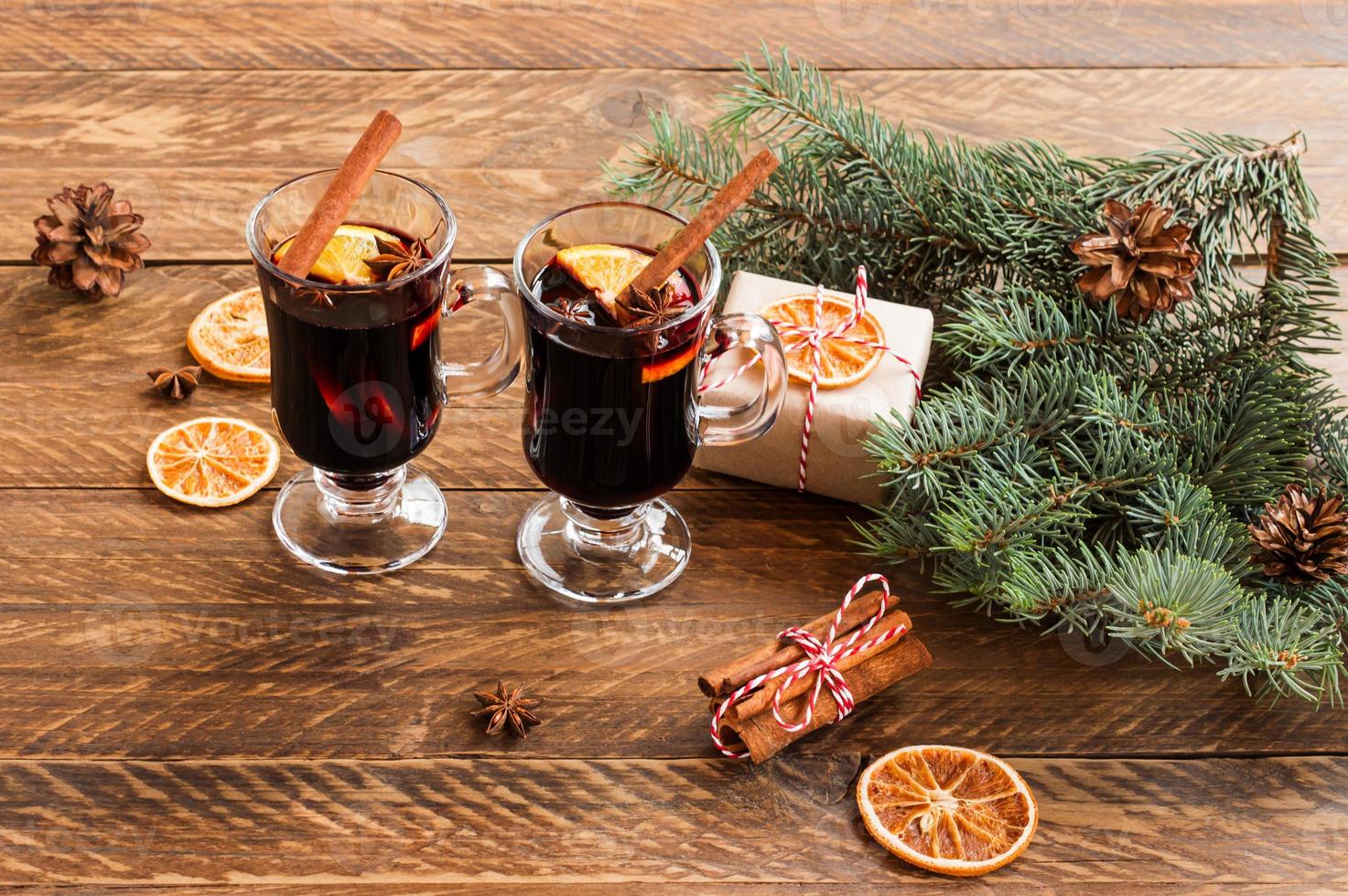 vino tinto caliente con especias. decoración navideña con rodajas de naranja seca. palitos de canela y regalos de Navidad sobre fondo de madera foto