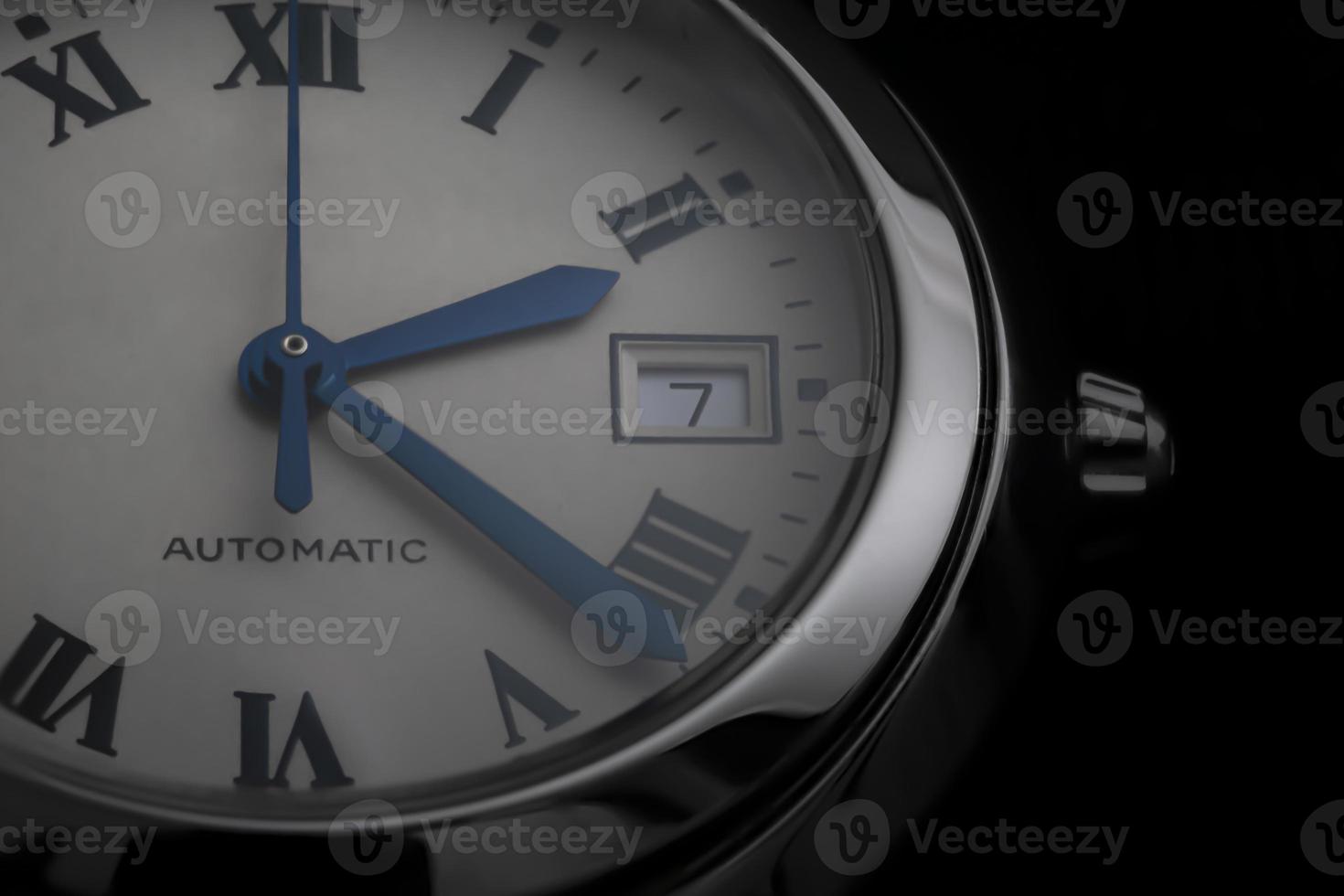 Close-up of an automatic Swiss watch with blue hands, date window and steel round case photo