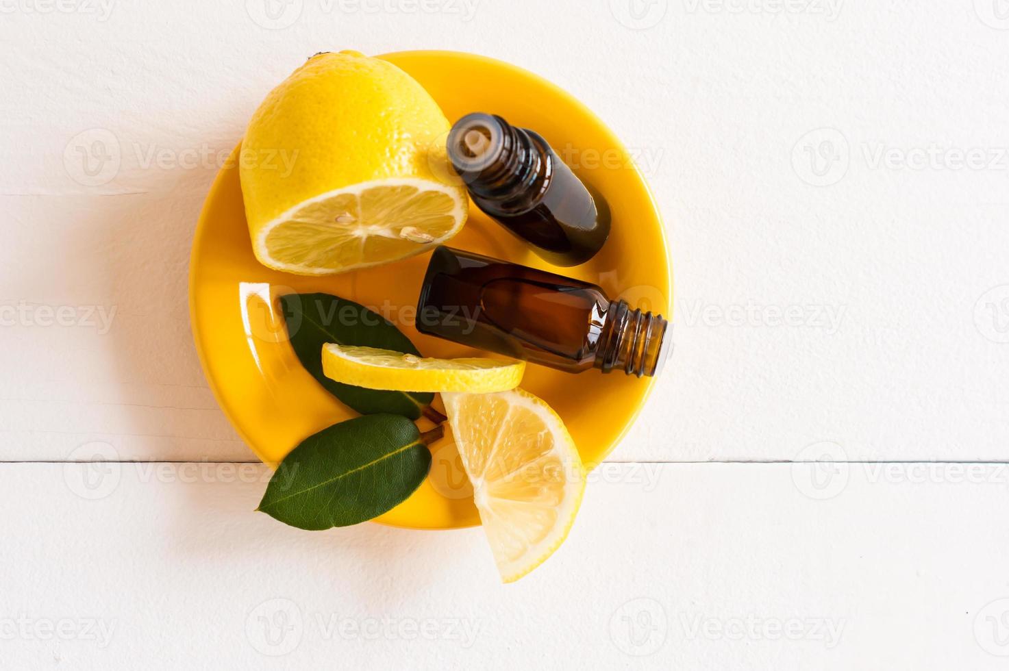 cosmetic oil or lemon essential oil in two bottles with a dispenser on a yellow plate with slices of lemon fruit. white wooden background. photo