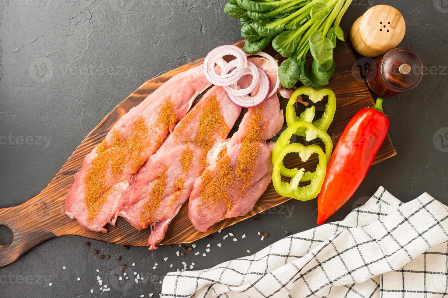 chuletas de cerdo listas para freír de carne de granja en una tabla de cortar de madera con especias para hornear. fondo negro. vista superior. foto