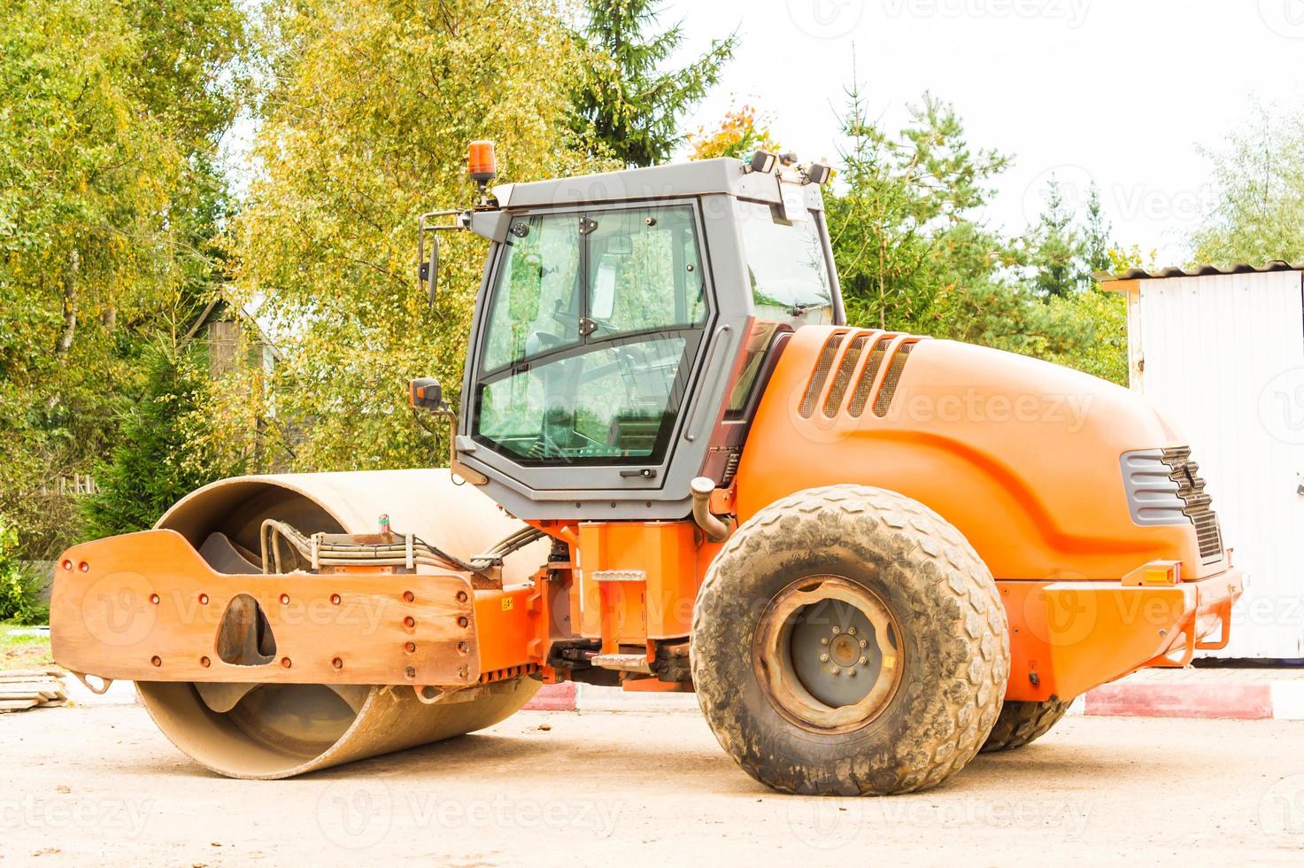 orange asphalt roller in the parking lot before the start of construction work on laying bitumen. machine for compaction loose building materials. photo