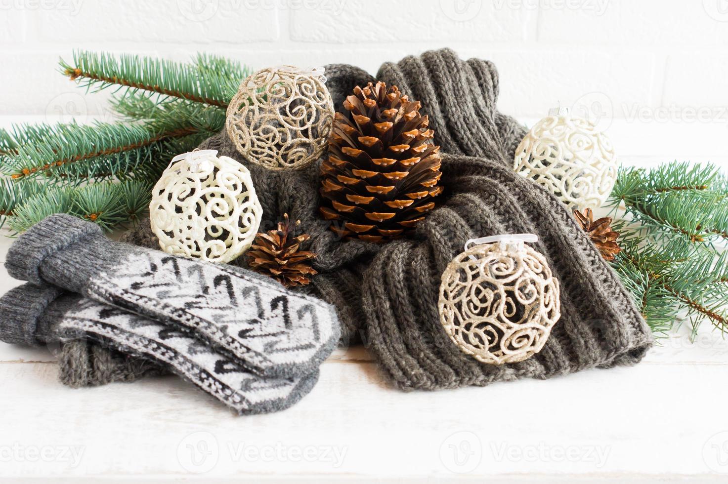 knitted warm scarf and mittens in the composition with openwork balls, cones and branches of spruce on a white background. the concept cozy Christmas. photo