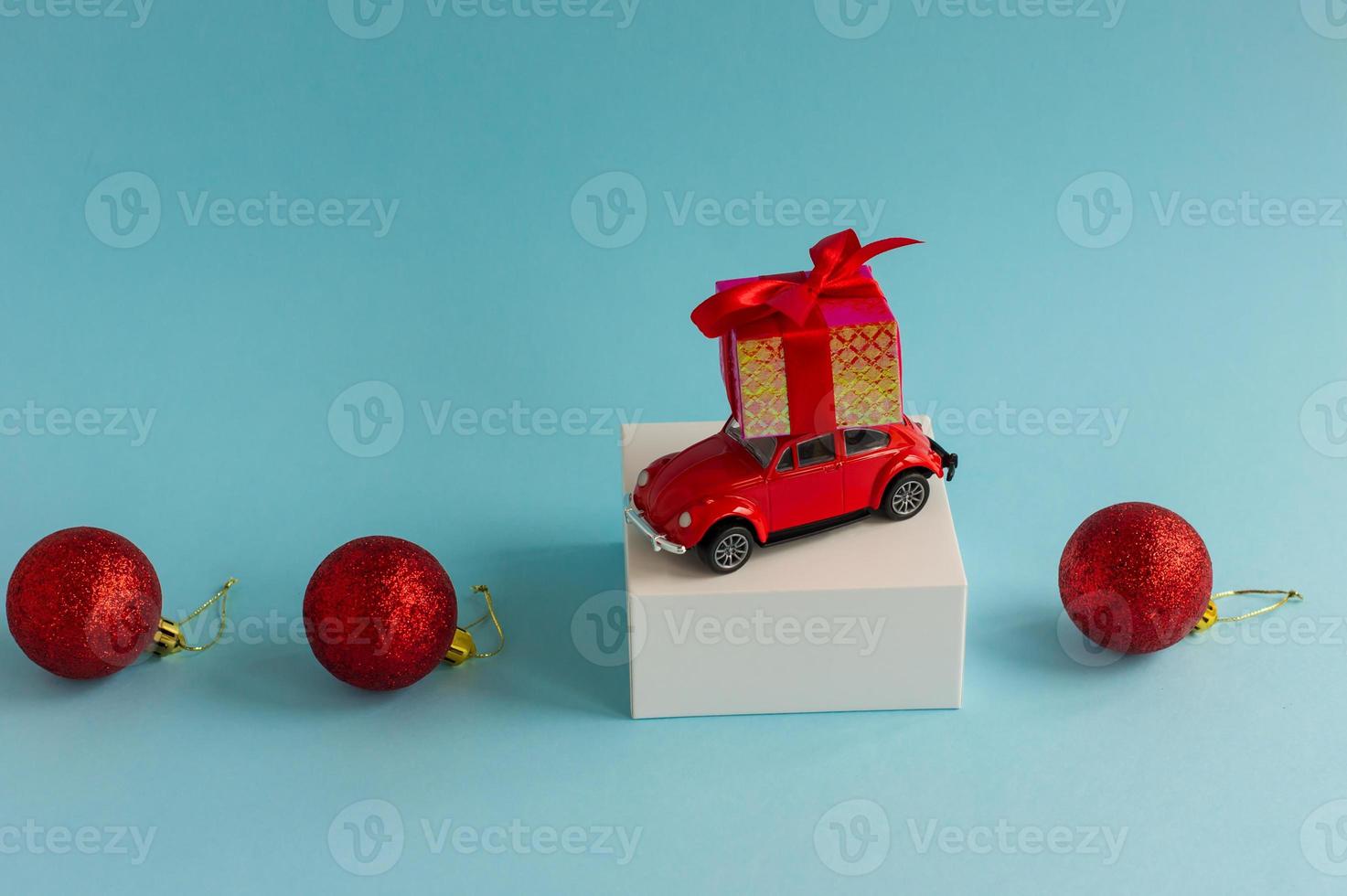 a miniature model of a red car with a New Year's gift on the roof against a blue background with three red balls. a copy of the space. photo