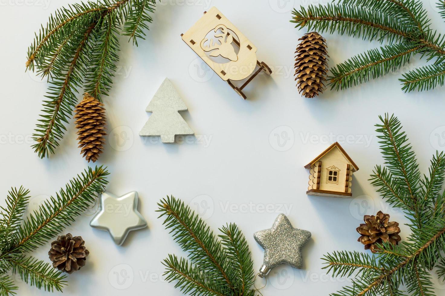 fondo festivo de año nuevo con conos y ramas verdes, estrellas plateadas, trineos de madera y una casa de juguete. diseño plano. vista superior. foto