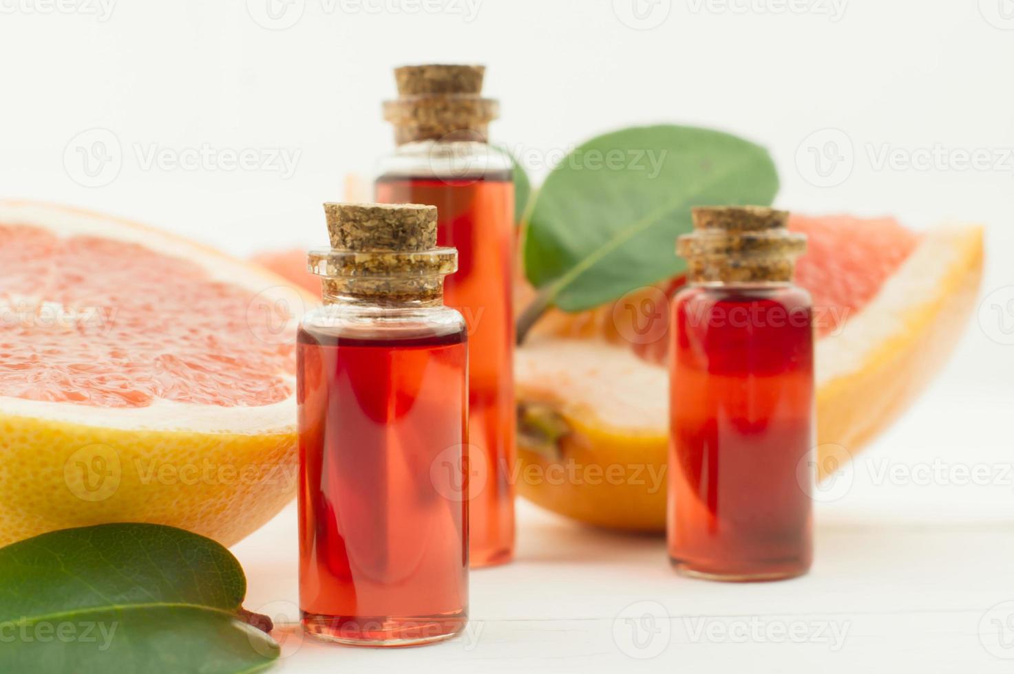 aceite esencial de pomelo aromático en tres botellas con tapa de corcho. frutos maduros y hojas. Fondo blanco. foto