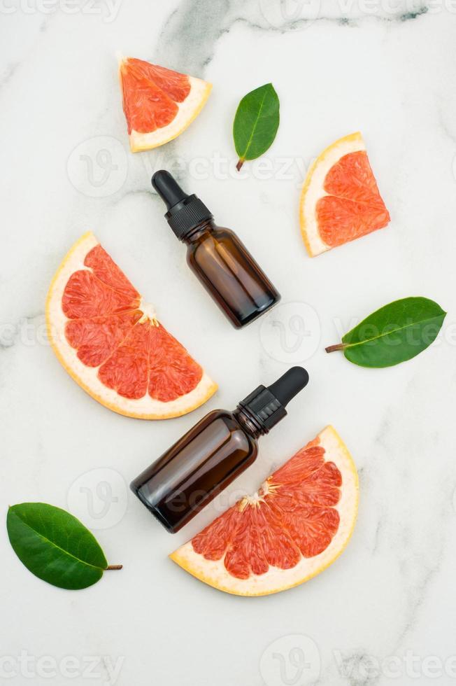 flat layout. two bottles of droplets with grapefruit oil and slices, leaves on a marble white background. top view. photo