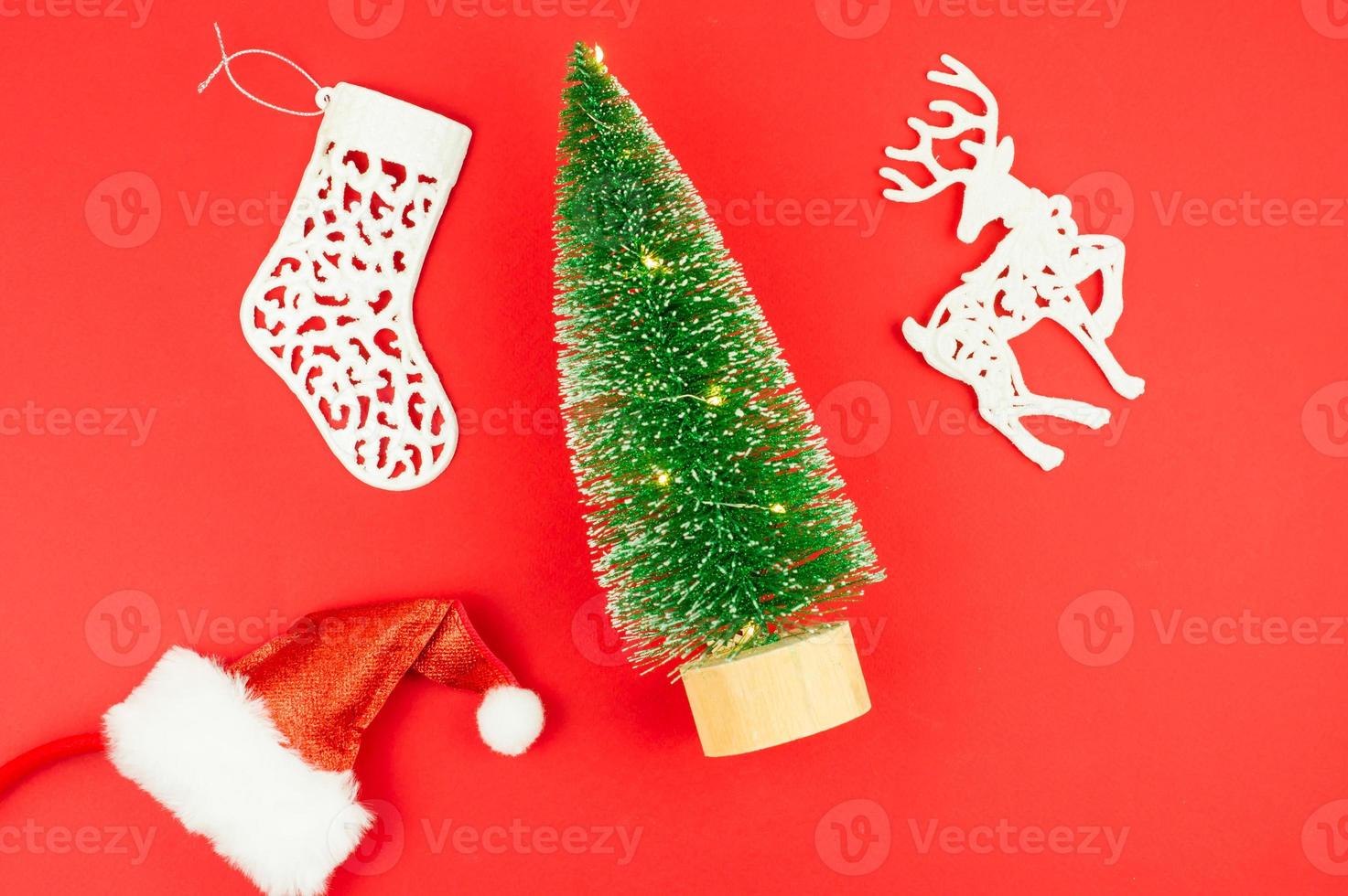 flat layout. top view. on a red background, a toy tree with lights, a santa hat, a white deer and a Christmas sock. photo