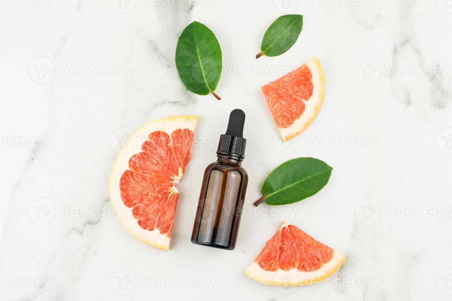 bottle with a dispenser made of dark glass with cosmetic oil or grapefruit essence on a marble background. top view. cosmetic self-care. photo