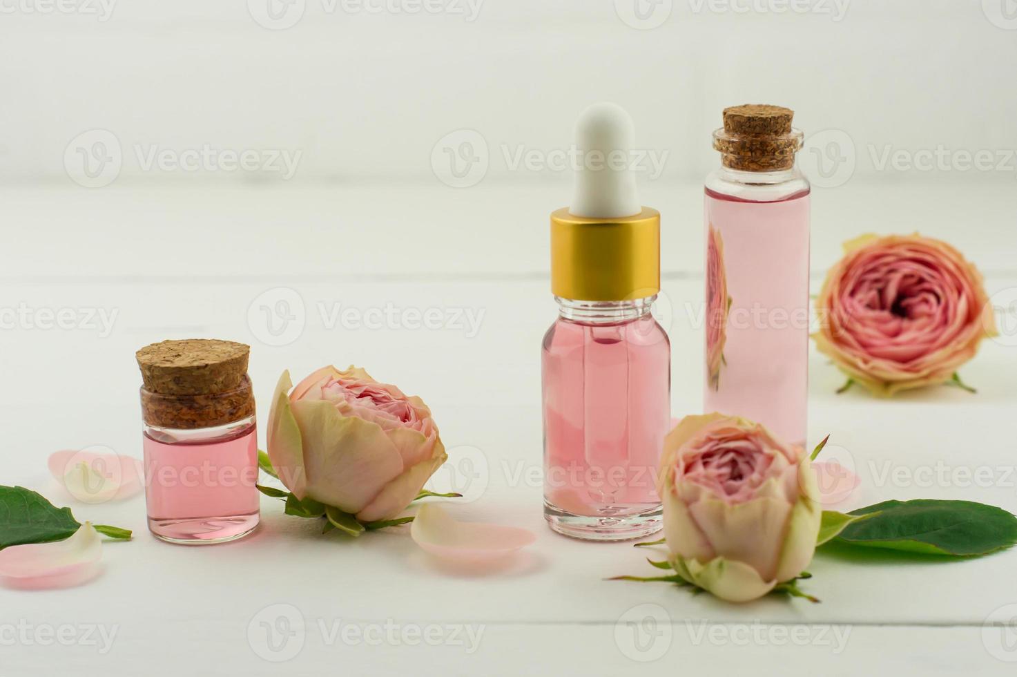 aceite facial de belleza hecho de flores de rosa sobre fondo blanco de madera con flores frescas. cuidado de la piel tratamiento facial y corporal. aromaterapia foto