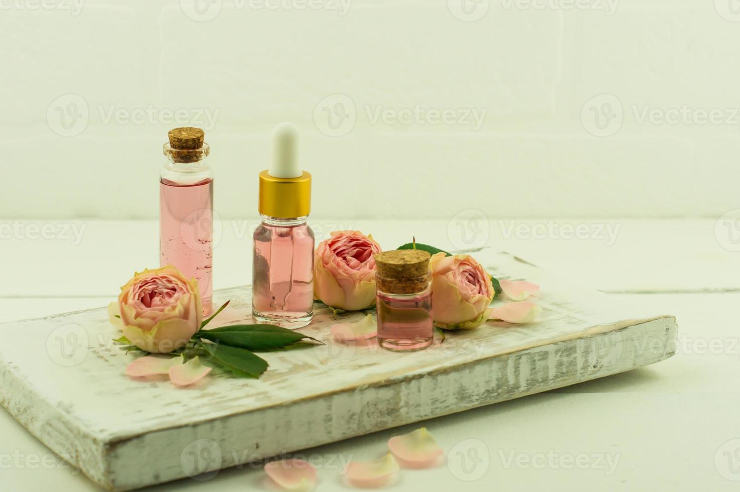 white wooden pouill with glass bottle with cork lid and pink essence, cosmetic bottle with rose oil. photo