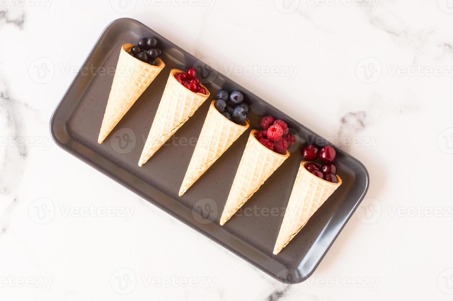 waffle cone with frozen currant berries isolated on white background, concept of juicy ice cream, close up. photo
