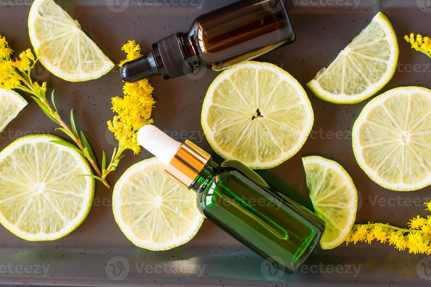 moisturizing oil-fluid for the face with citrus extract in bottles with a pipette against the background of slices of lemon and sprigs of solidago. photo