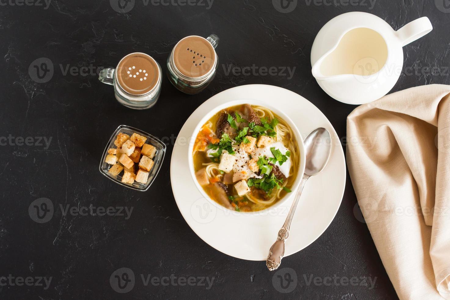 seasonal summer soup of forest mushrooms with cream, greens and croutons. delicious lunch. black background. top view. photo