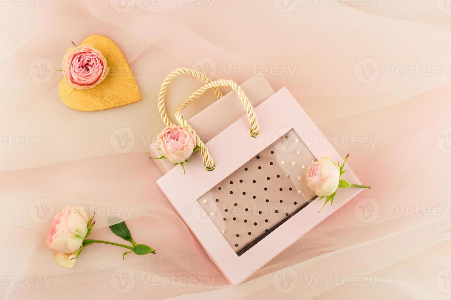 Valentine's Holiday. Beautiful gift box in a festive bag on a pink pastel background veil with buds of live roses. A gift with love. photo