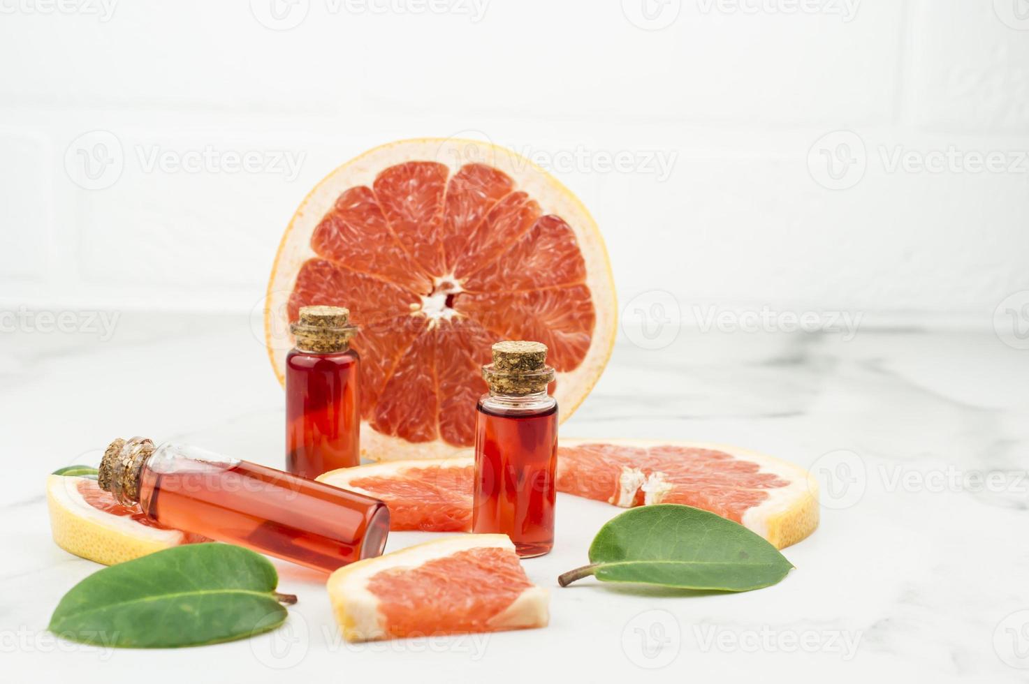 three glass bottles with a stopper with oil or grapefruit essence on a marble background with fruit slimes. the end of natural self-care. photo