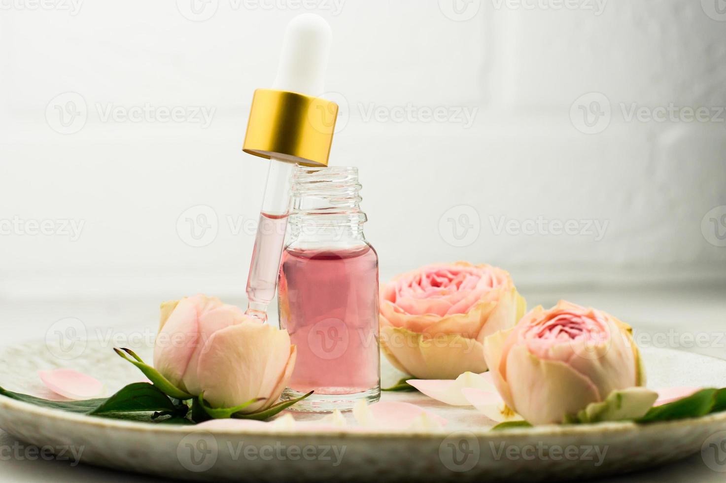 an open bottle of rose oil and a pipette filled with cosmetics for rejuvenation and facial skin care on a ceramic plate. photo