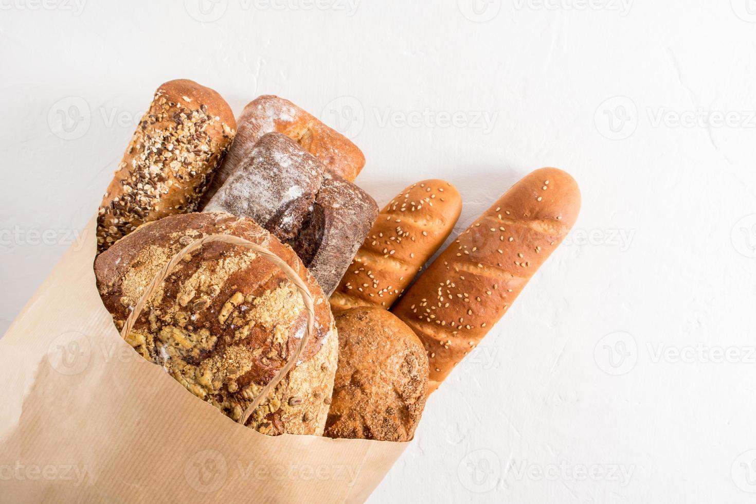 Kraft bag filled with various types of bread from the bakery. Zero waste, eco shopping and delivery. white background. photo