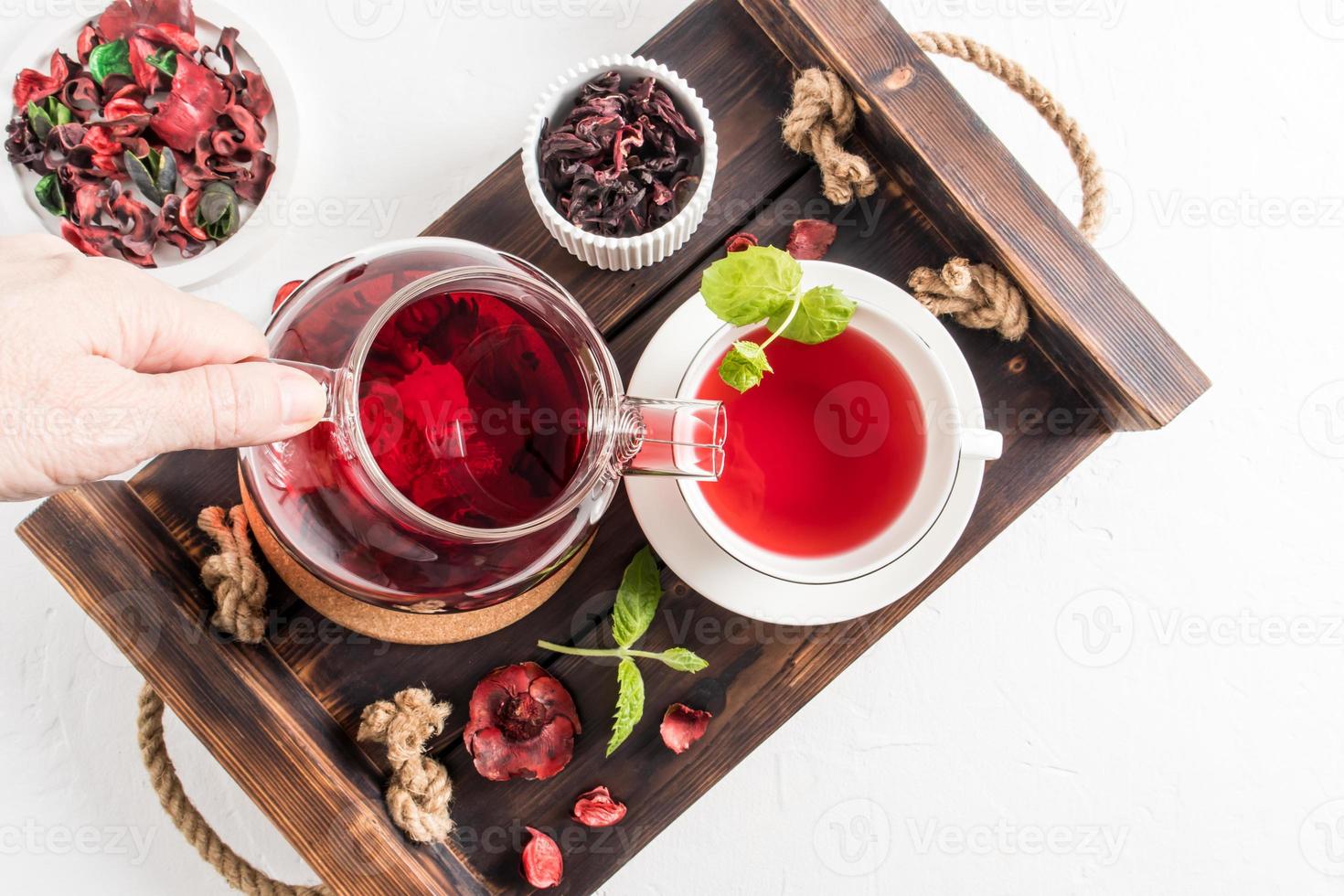 tea ceremonia . a woman's hand pours fragrant red hibiscus tea into a cup of mint leaves. top view of the wooden tray with morning tea. photo