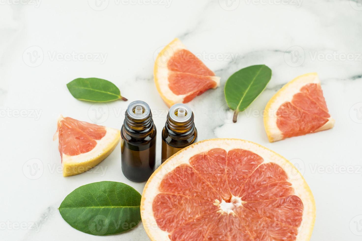two medical bottles with a dropper with grapefruit essential oil on a marble white background with grapefruit fruit, green leaves and sweets. photo